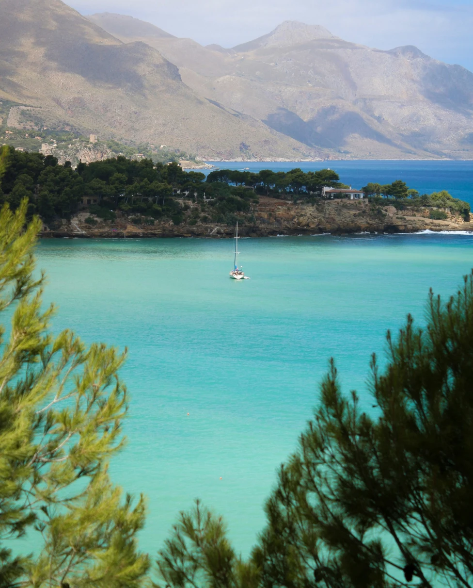 Sailboat off the coast with rocky outcroppings at daytime.
