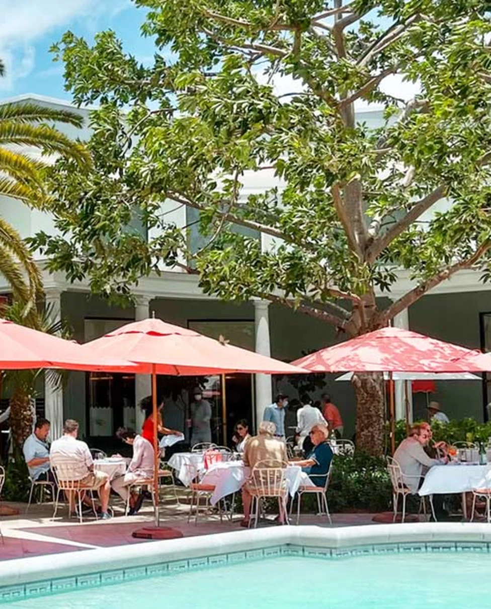 A view of a pool at a shopping center with plam trees and lovely sun umbrellas.