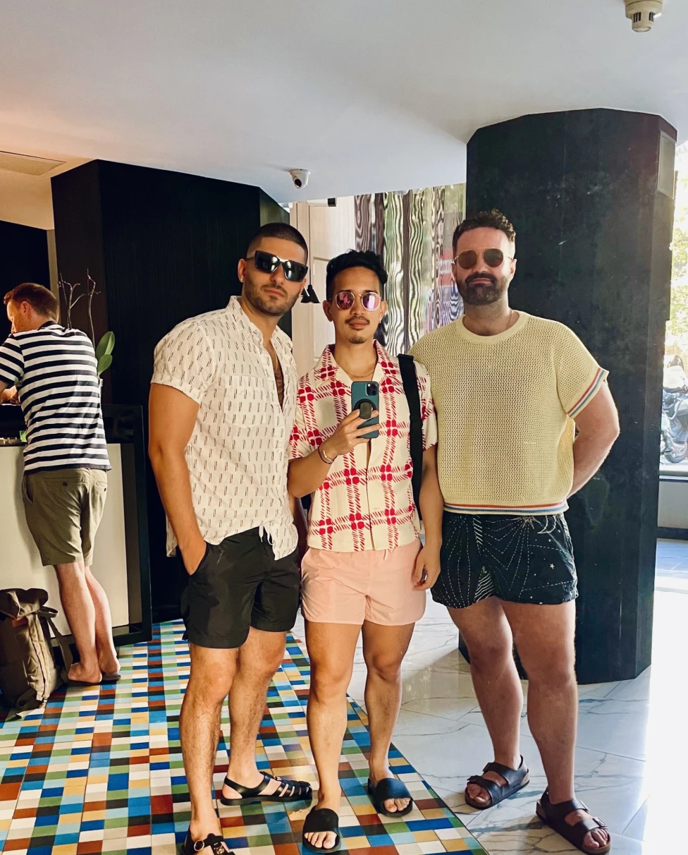 Three men dressed in tshirts and shorts, wearing sunglasses, standing on a colorful floor.