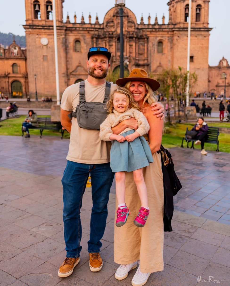 Three individuals stand in front of a historic church with a bustling square in the background.