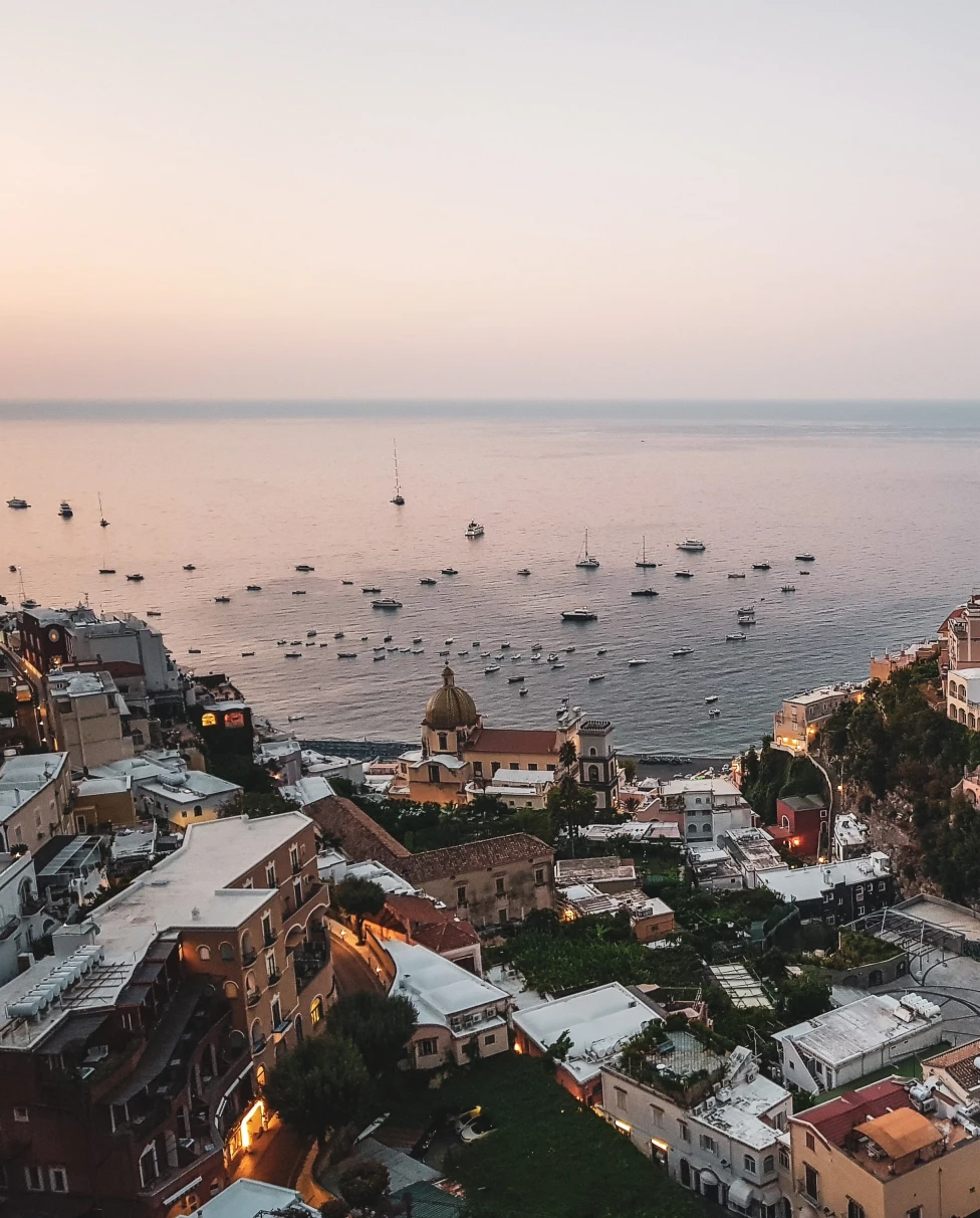 boats in the water next to cliff with buildings during sunset