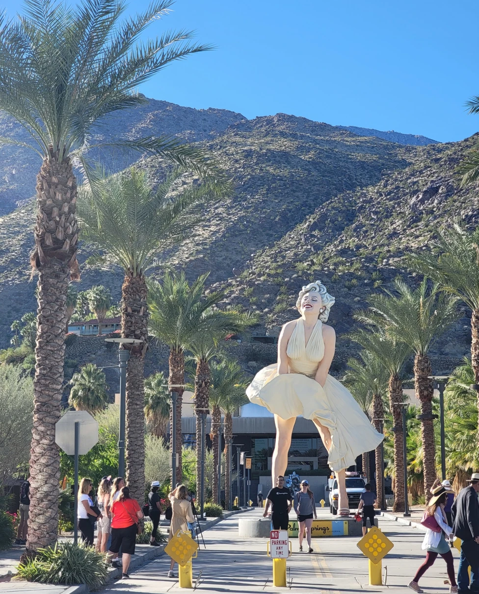 Statue of Marilyn Monroe between palm trees and in front of mountains.