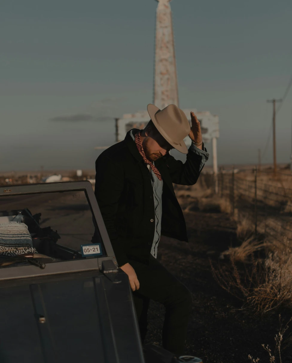 A picture of a man holding tipping a cowboy hat in front of a Texan monument.