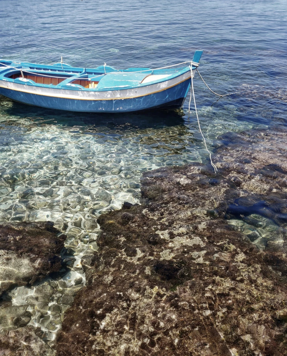 A small fishing boat drifting in the beautiful crystal clear water off the shore with rocks.