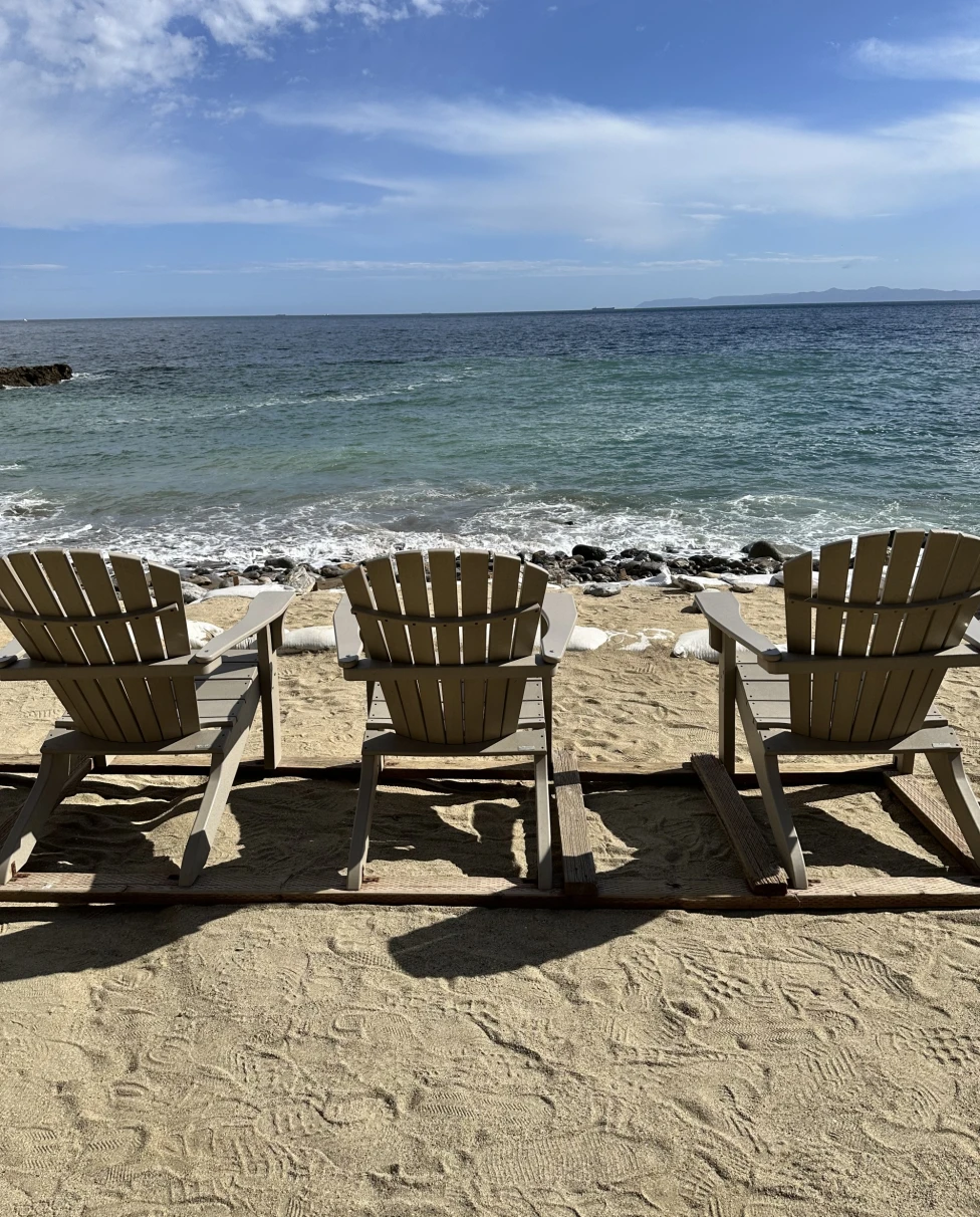 Three lounge chairs sitting on a beach in front of the water during daytime