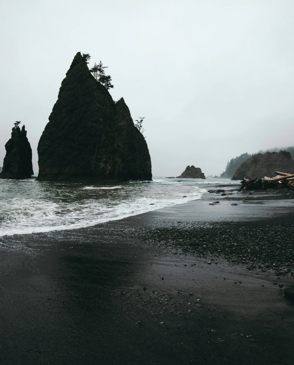 Black sand beach on a cloudy day with rock formations in the water