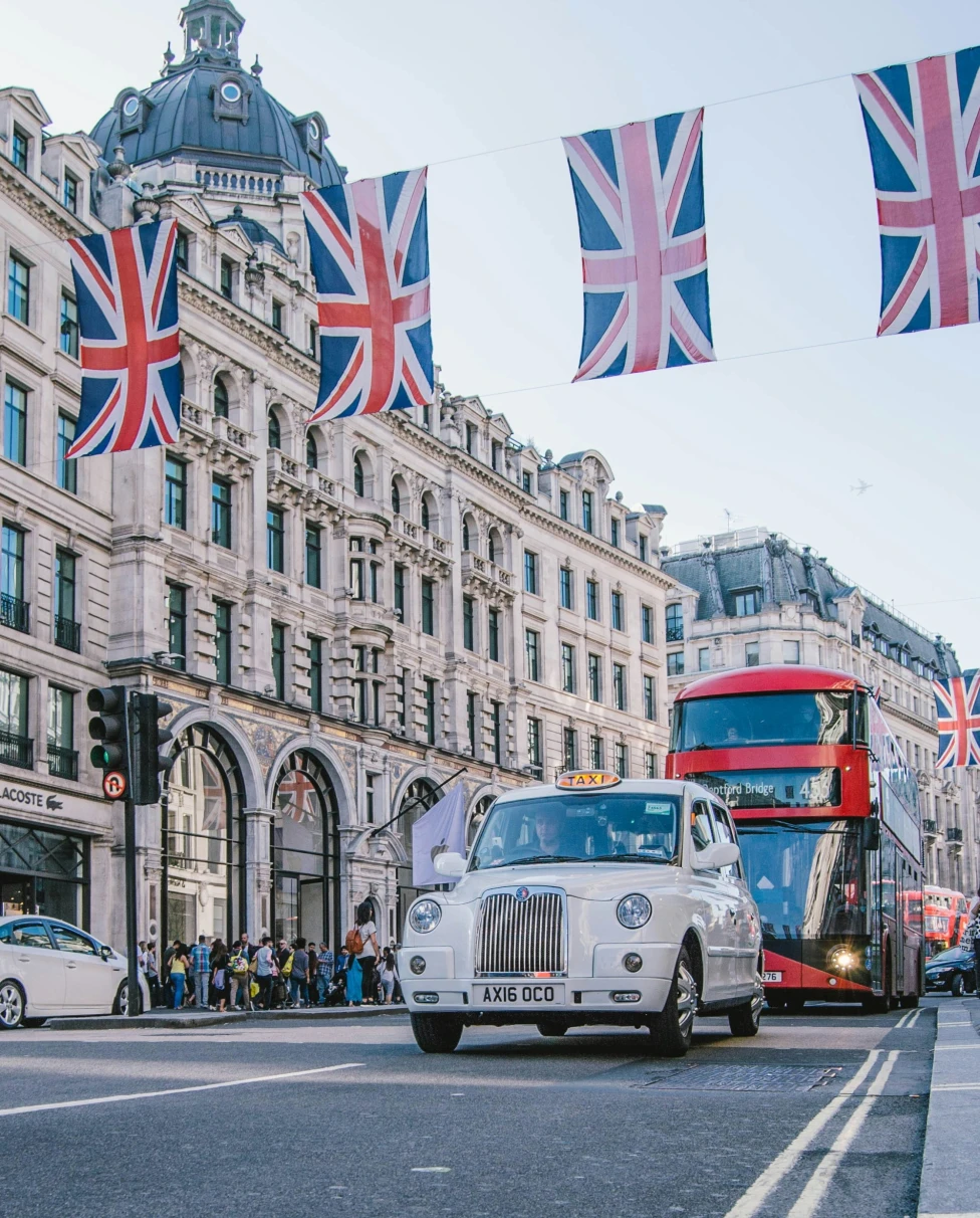 Street with red bus, car and flags on top.