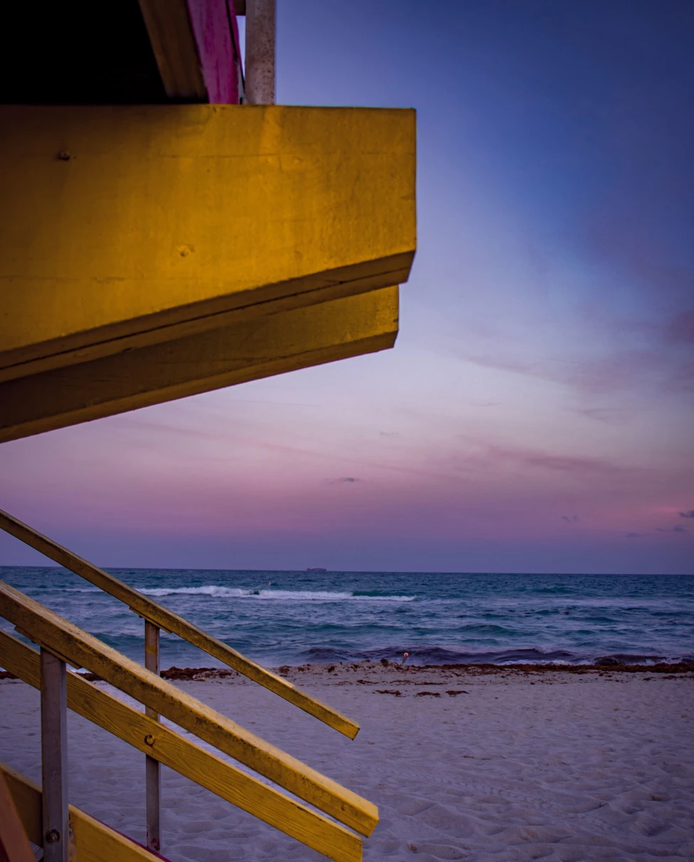 purple sunset on the beach next to yellow lifeguard stand
