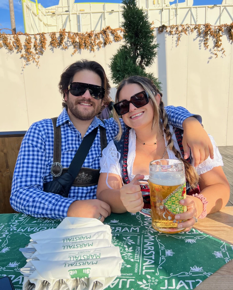 Couple posing in traditional Oktoberfest outfits with beers.