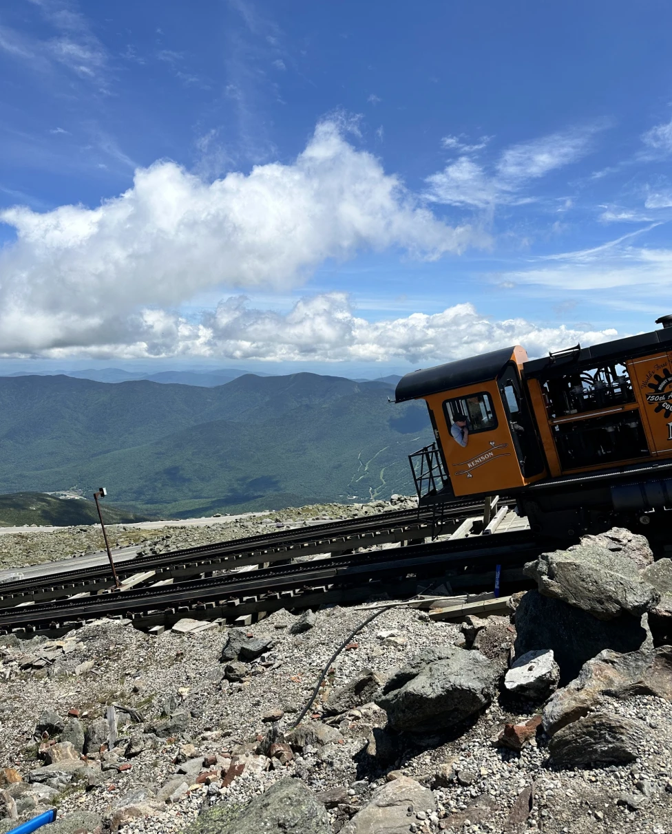 A cogwheel train ascending a mountain track under a clear blue sky.