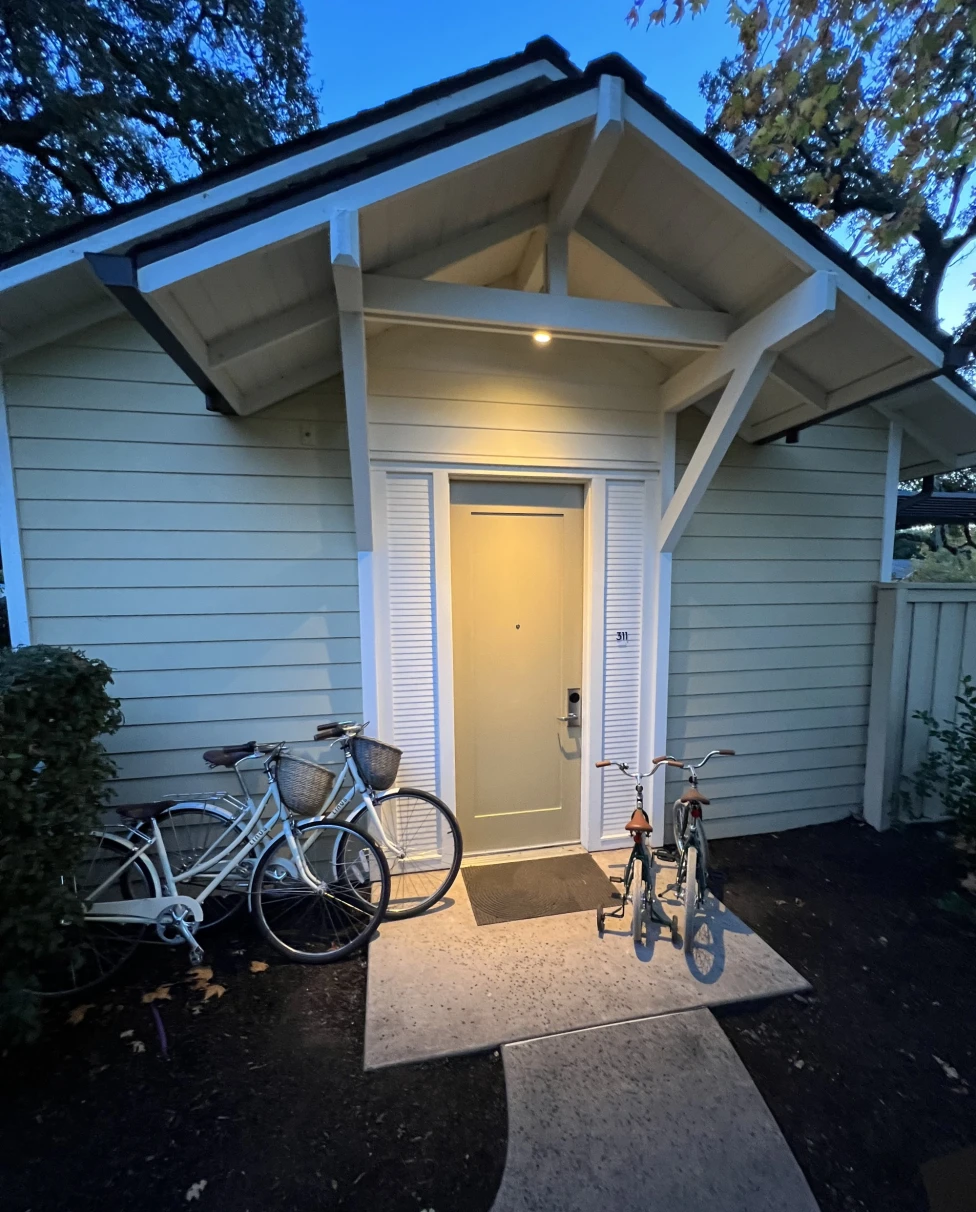 A white house with an illuminated yellow door and bikes on the front step.