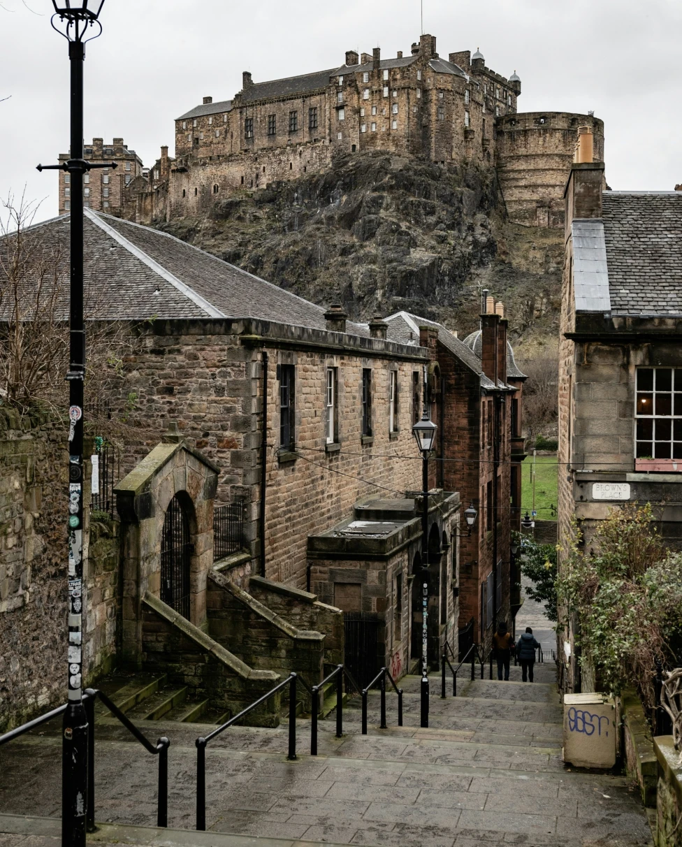 The image presents a picturesque cobbled street leading to an imposing castle atop a hill, with an old street lamp standing guard under overcast skies.