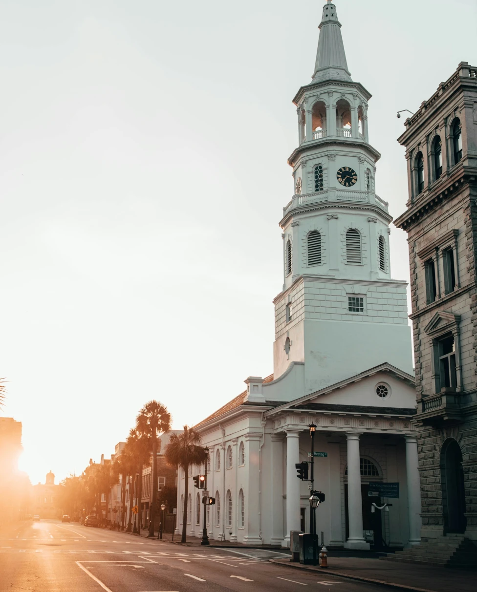 A tall, white church in a city street during a sunrise