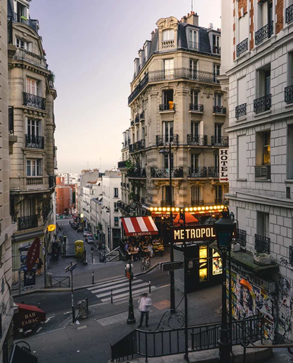 Street in Paris France with lit shops, white buildings and red yellow store fronts at sunset
