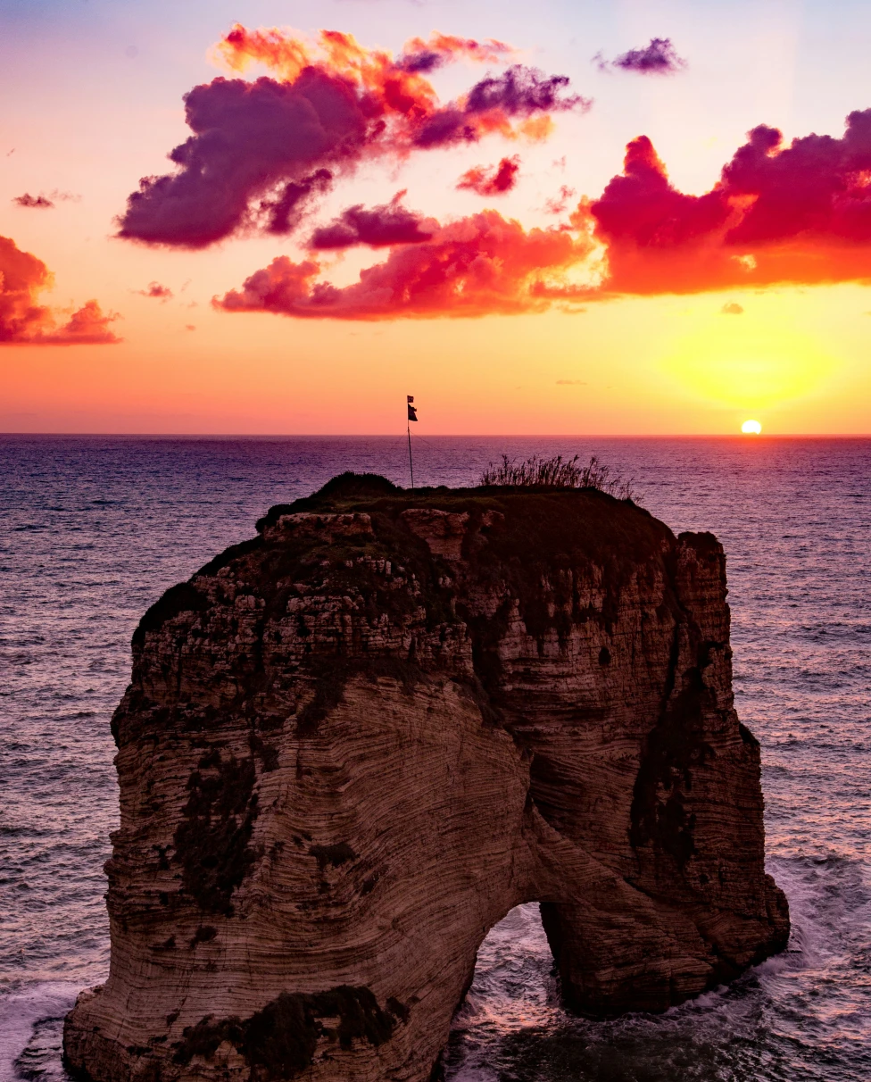 A purple and pink sunset over the sea and a large rock formation.