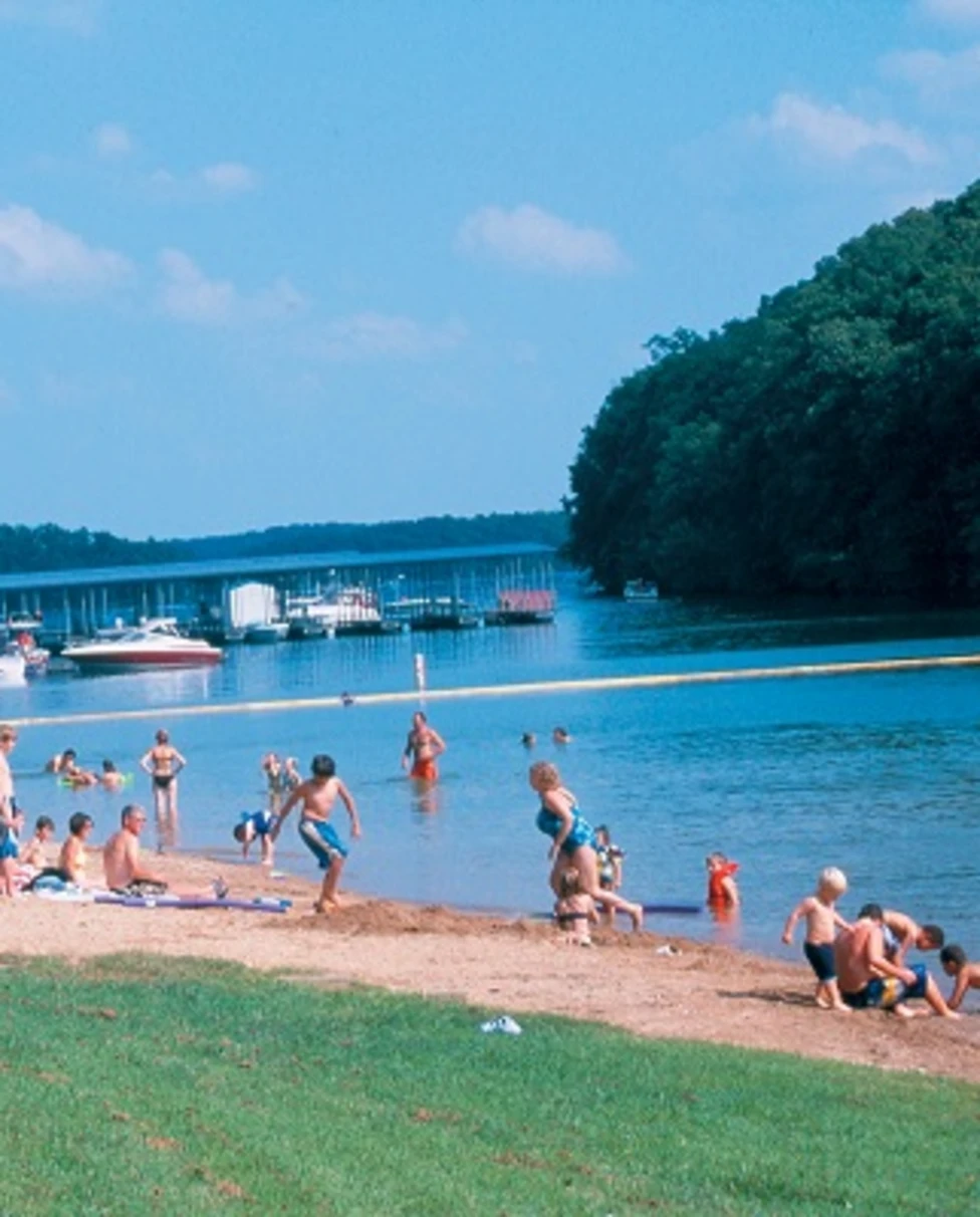 People enjoying the lake shore with boats in the distance and a clear sky.