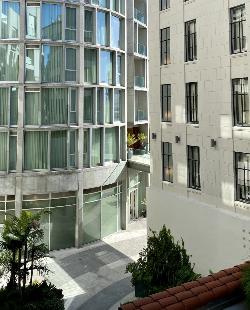 A view of white building exteriors with green trees on the ground.