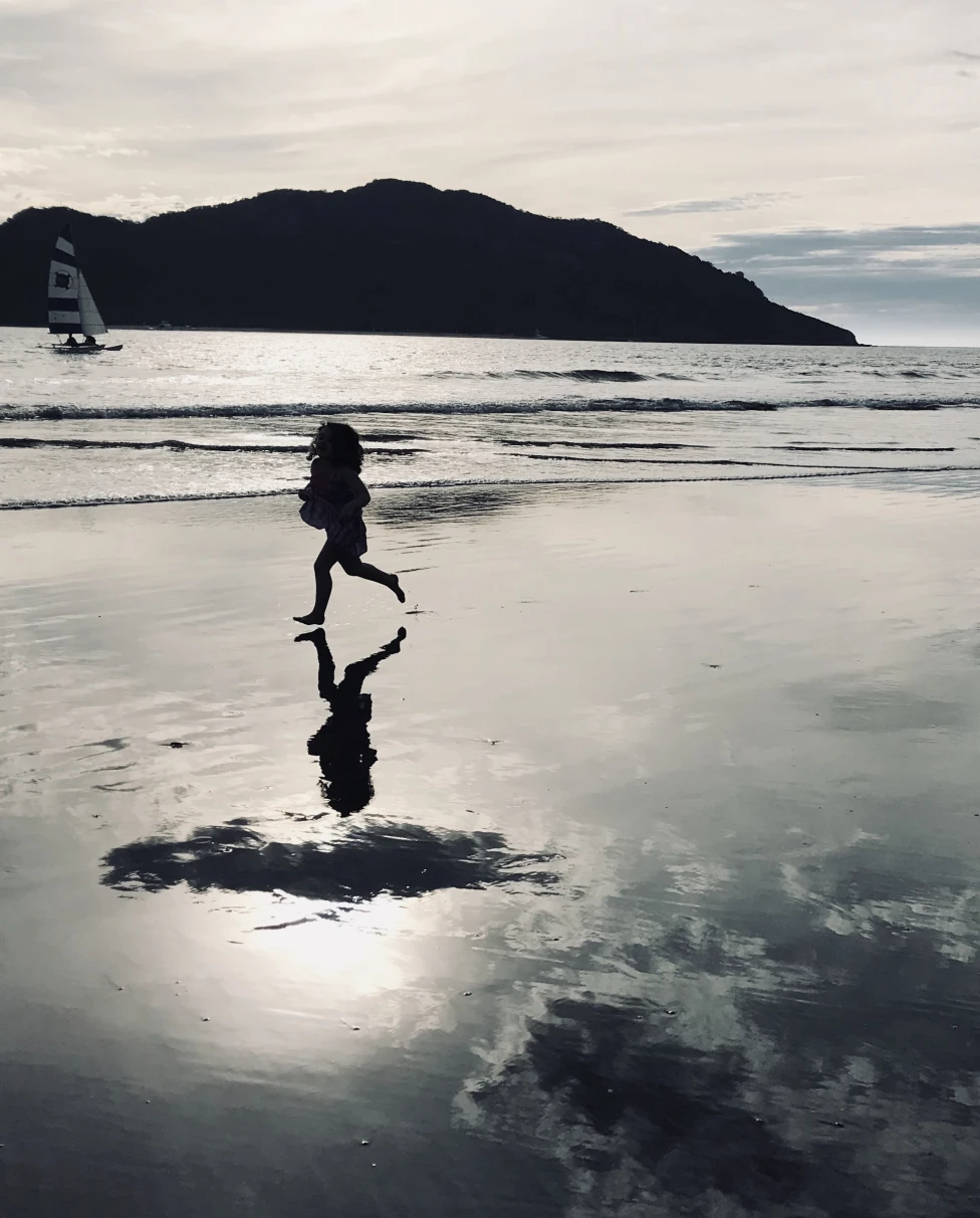 Two kids running on the beach with an ocean and a mountain in the background.
