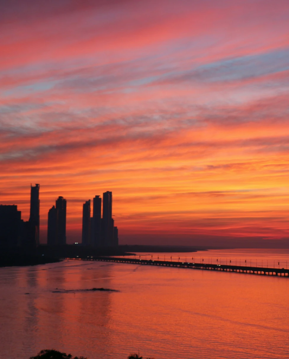A golden, pink and lavender sunrise over Panama City, over the water and a silhouetted skyline.