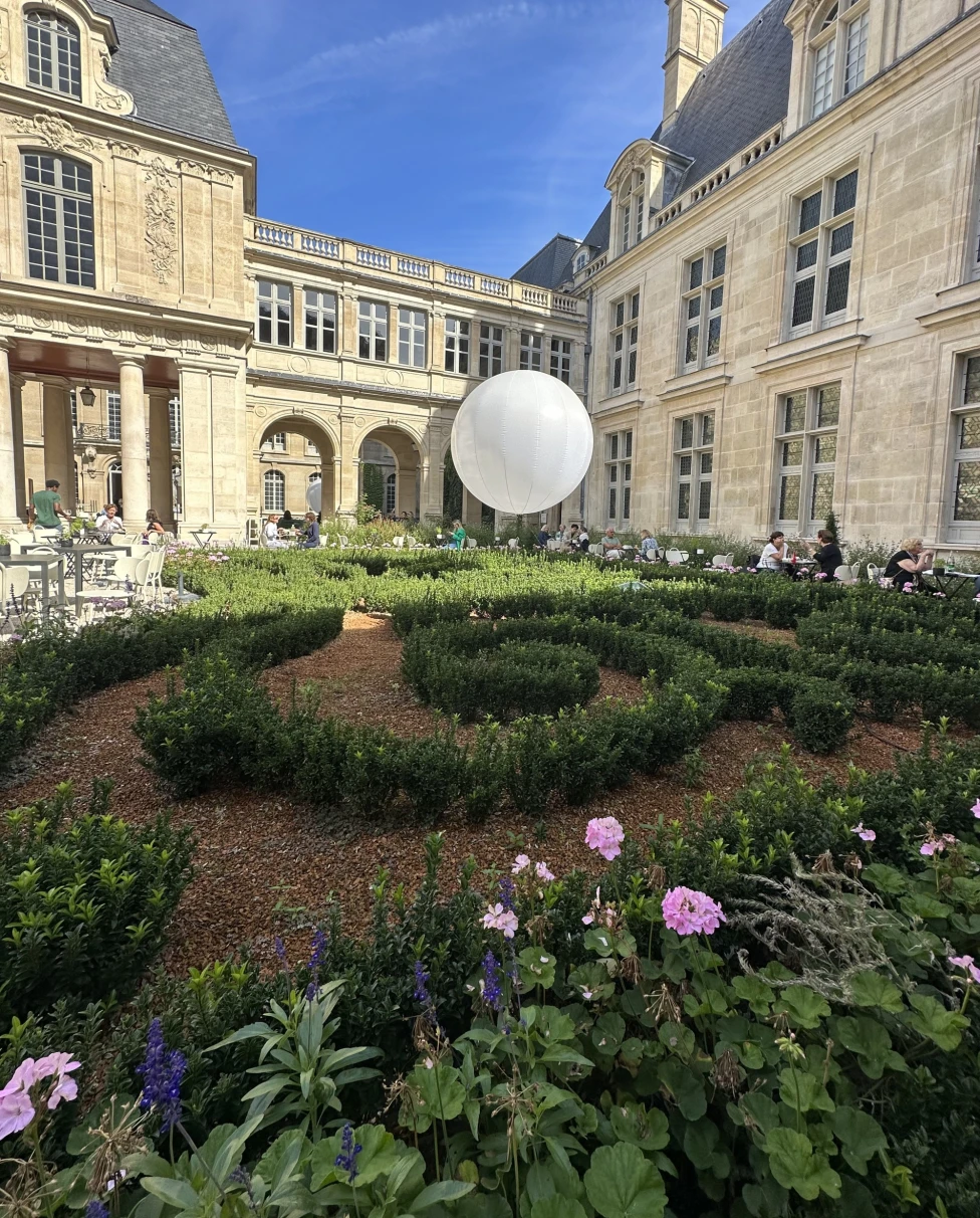 A garden with an architectural balloon surrounded by a beige French-style building during daytime.