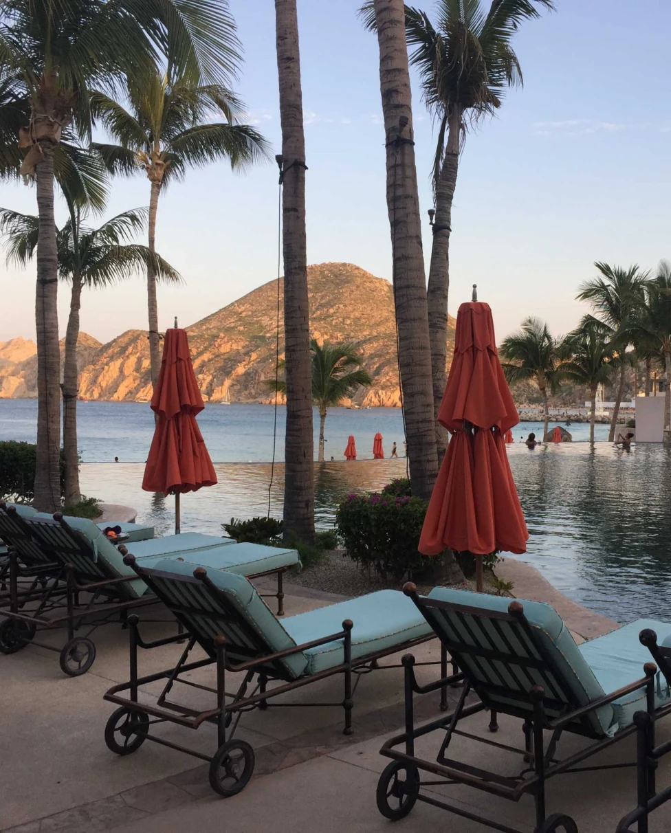Lounging chairs and red umbrellas near a pool area in a resort.