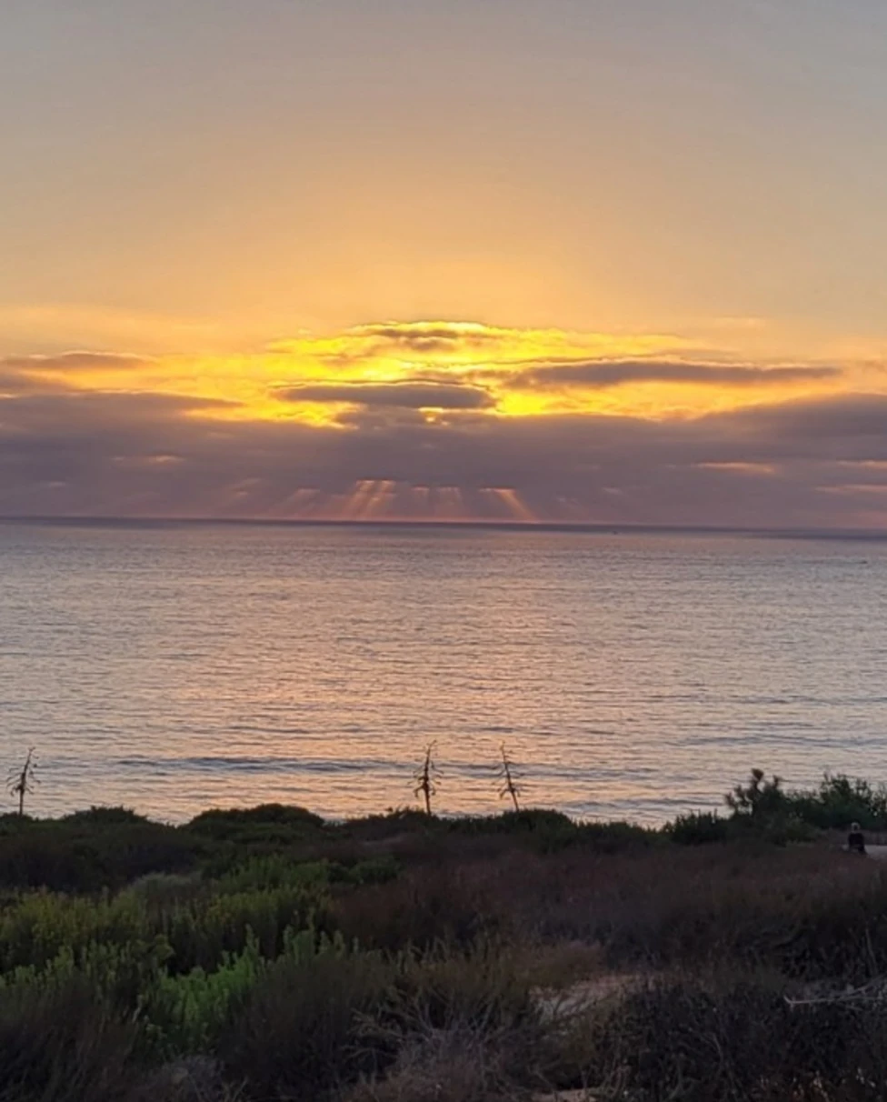 The image captures a stunning sunset over the ocean, with rays of sunlight piercing through clouds and reflecting on the water.