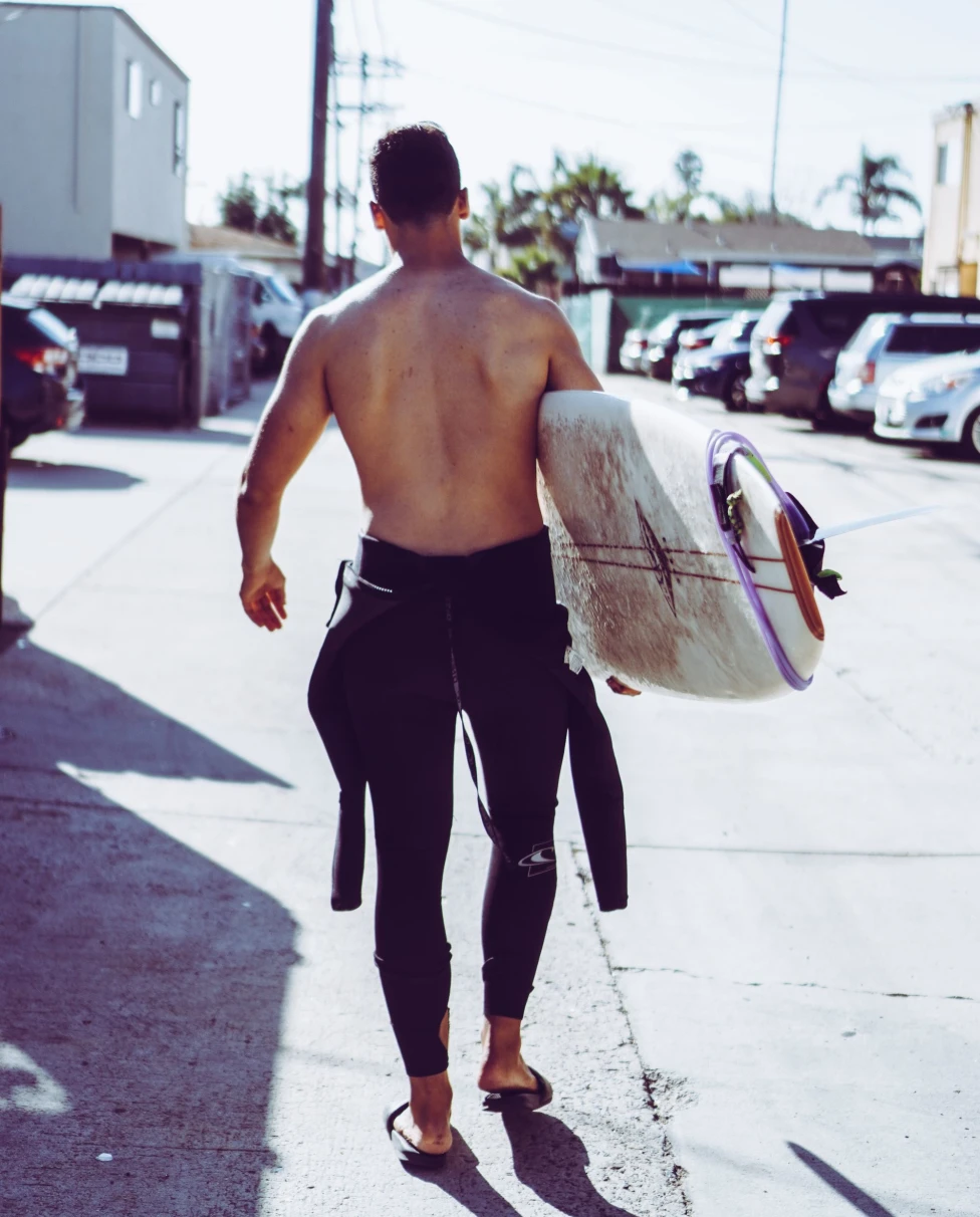 surfer walks with his surfboard down street