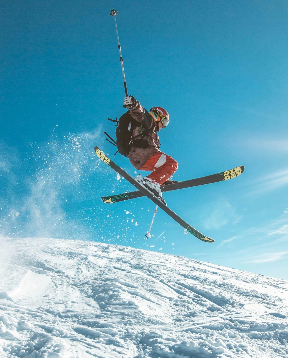A skier goes off a jump with a blue sky behind.
