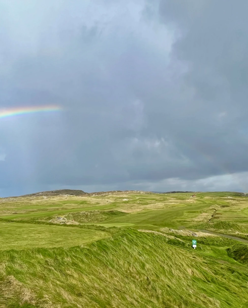 A picturesque landscape featuring a rainbow arching over verdant hills beneath a cloudy sky.