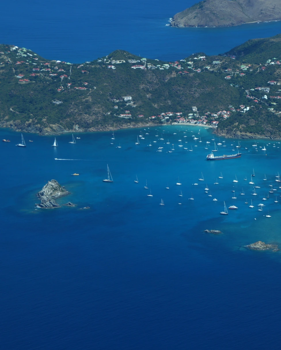 aerial view of saint kitts and nevis large blue ocean with multiple white boats and a large green land mass with pockets of homes
