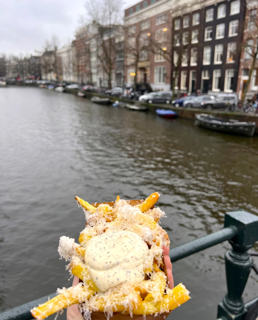 A person holding fries on a bridge in front of a row of buildings.