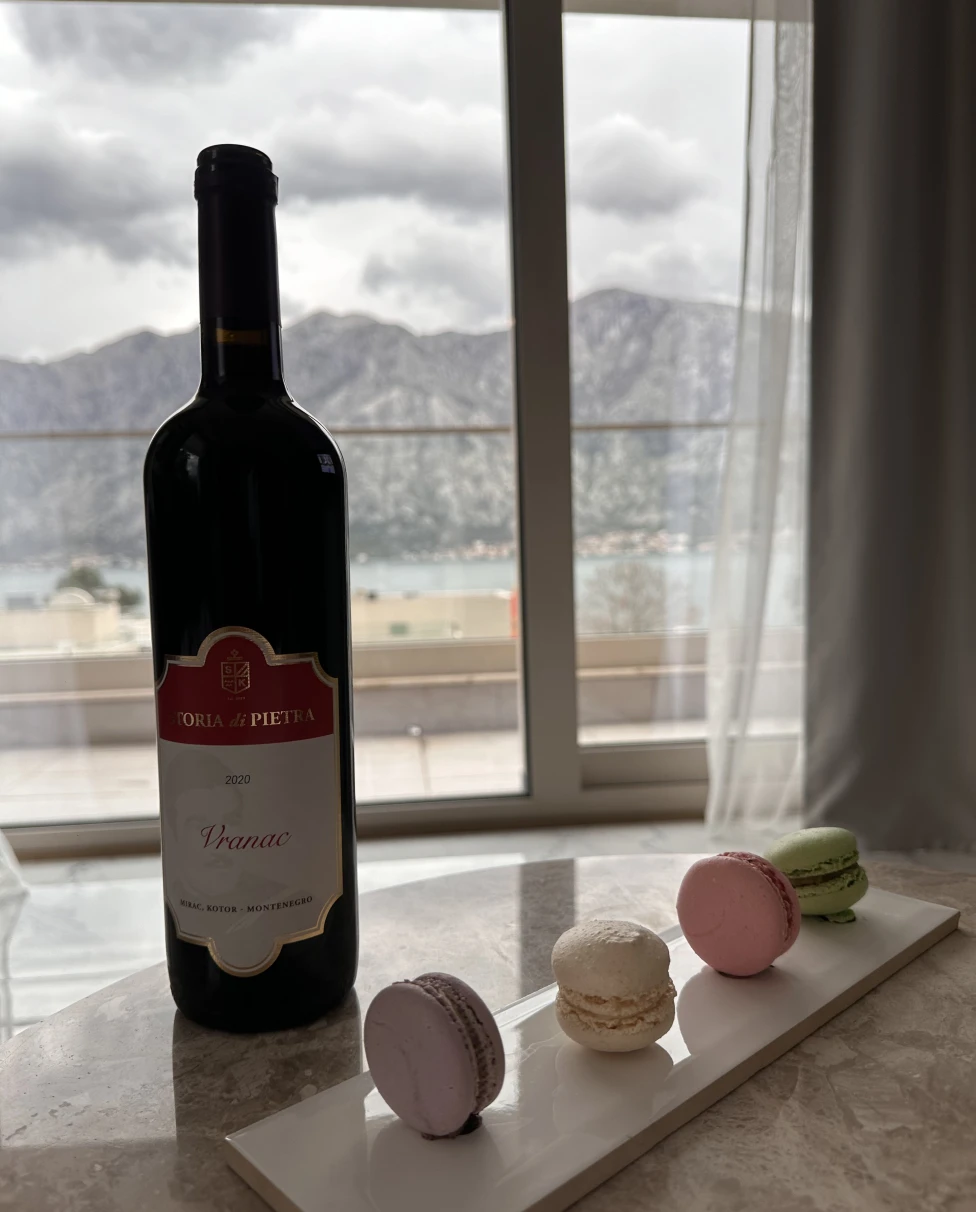 A picture of a bottle of wine and macarons on a white dish placed on top of a stone table.