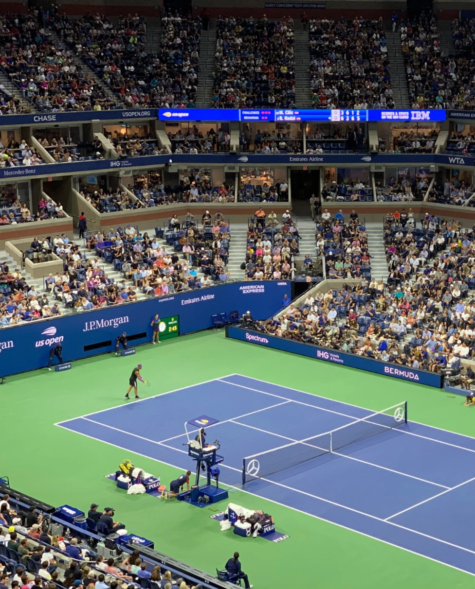 A tennis match with spectators, featuring a blue court, players in action, and professional tournament scoreboards.