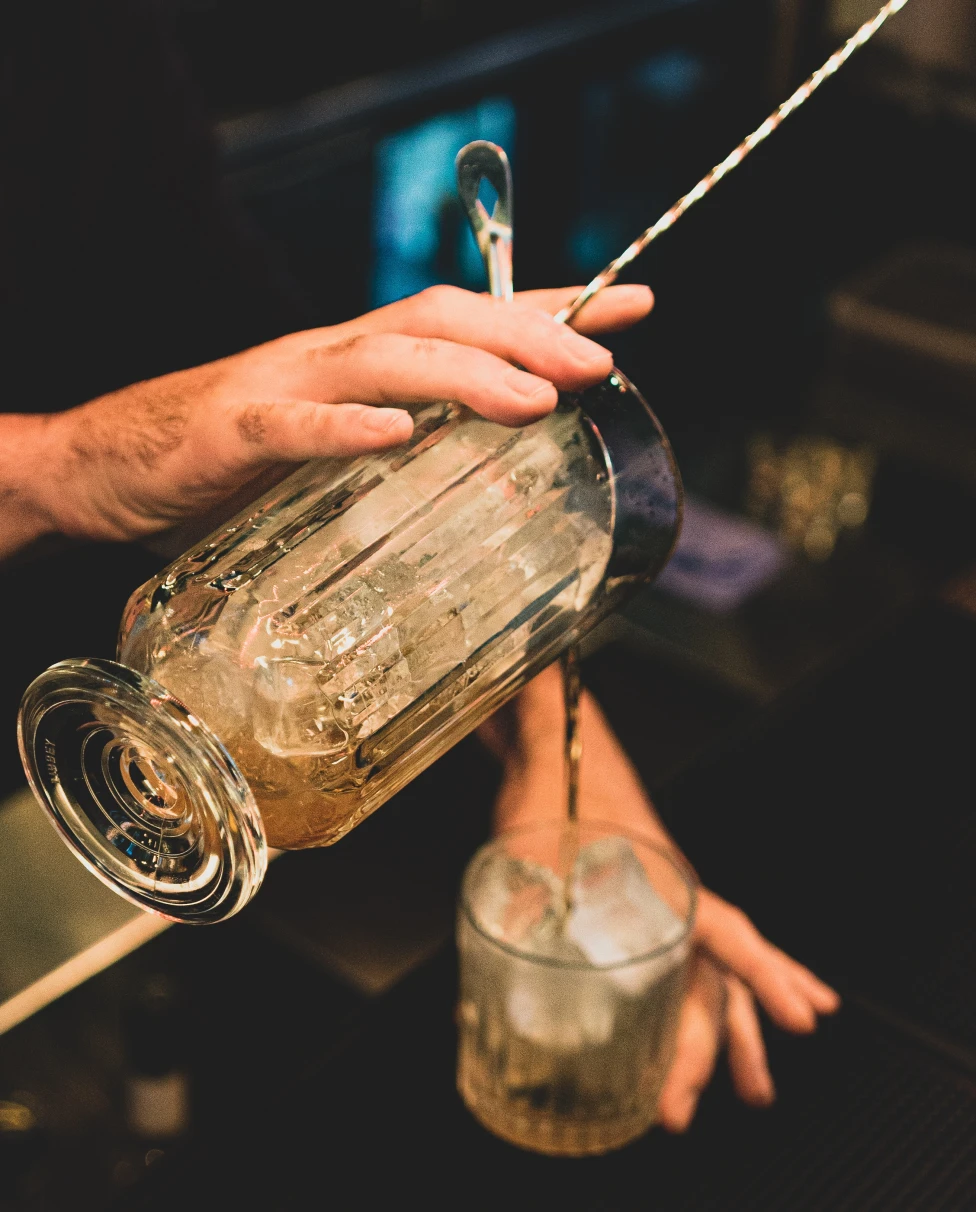 A bartender making a drink and pouring into cup.