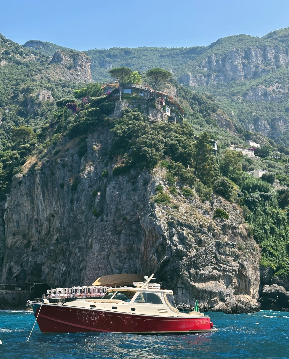 A picture of a red-colored ship on the water near an Island during daytime.