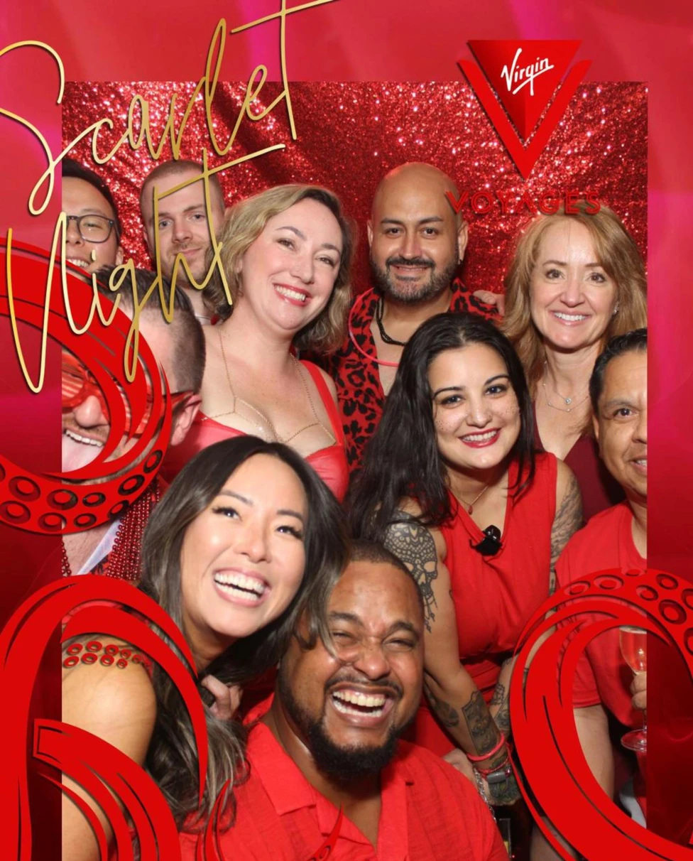 A group of smiling people dressed in red poses against a glittering red backdrop for a "Scarlet Night" event hosted by Virgin Voyages.