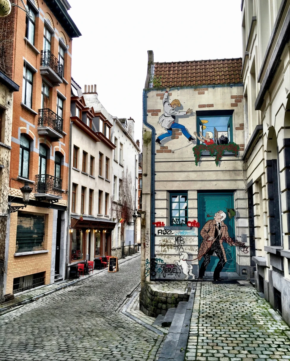 A brick street with houses with a lot of windows and painted murals in the surrounding areas.