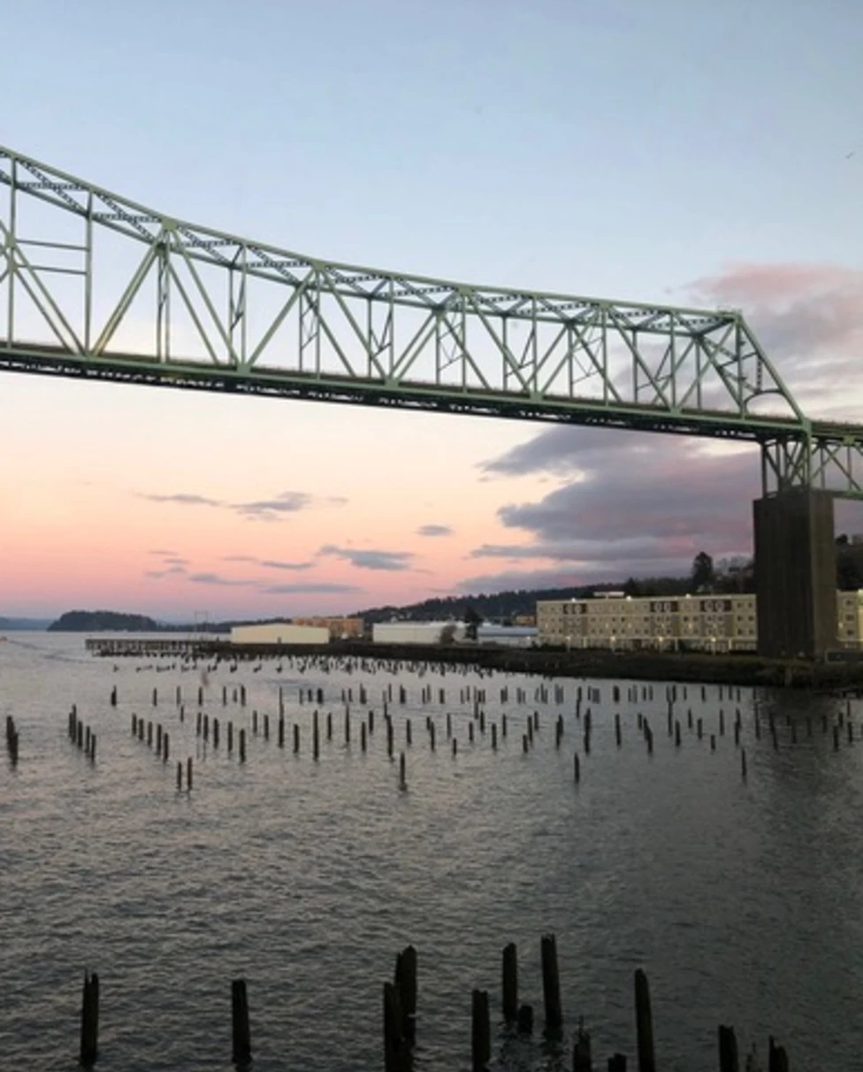 A green truss bridge over a body of water during the evening.