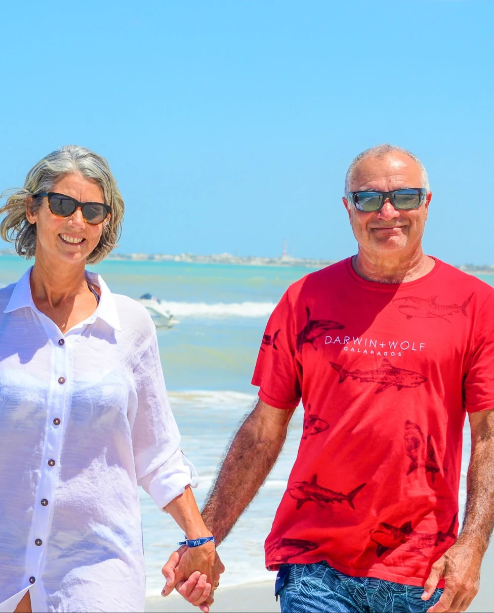 A man and woman walking on a beach holding hands.
