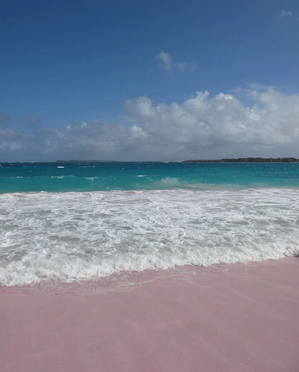 Blue water with white waves crashing onto pink sand in St. Martin in the Caribbean.