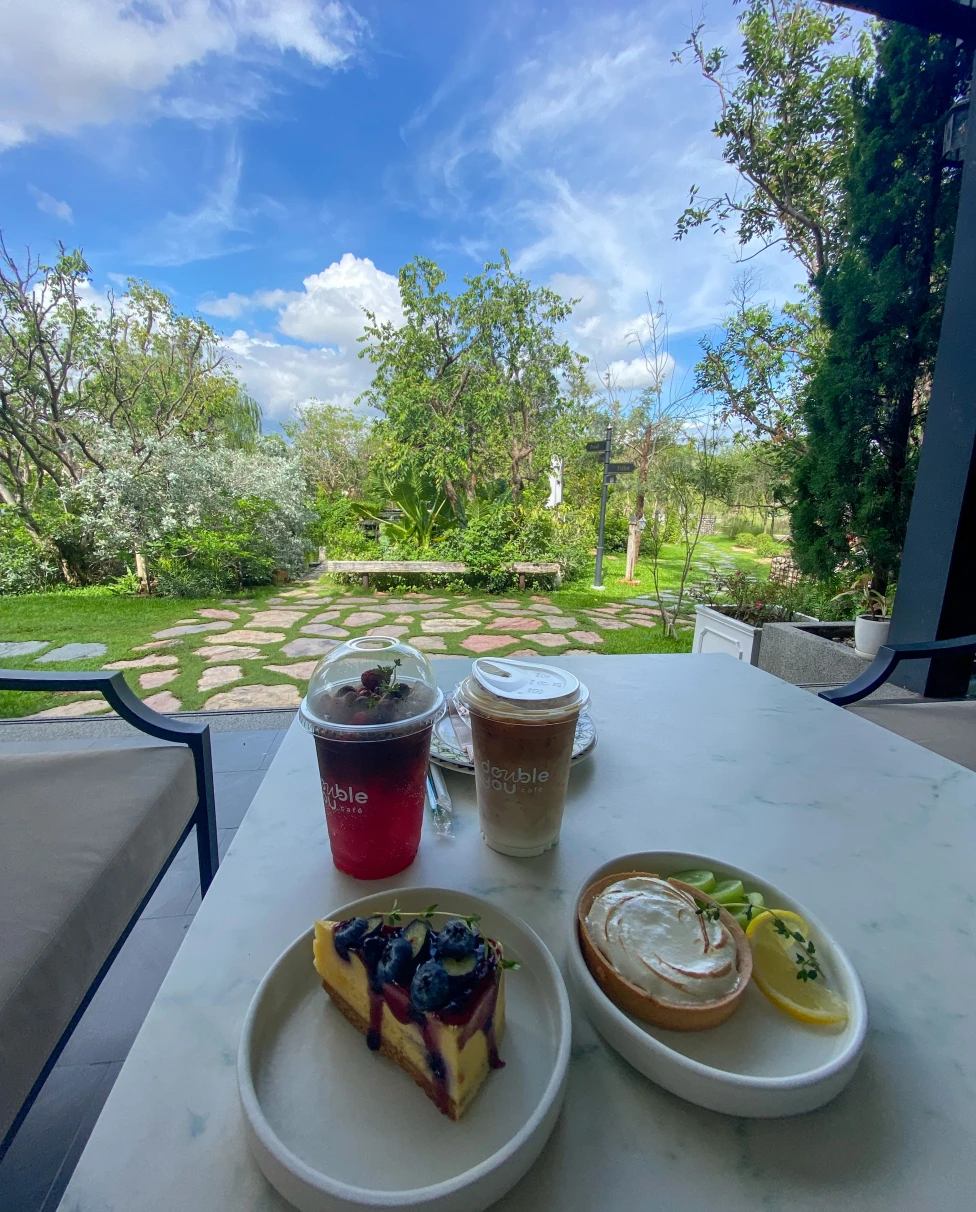 A patio table with two plates of breakfast pastries and two to-go coffee drinks overlooking a garden at Double You Cafe.