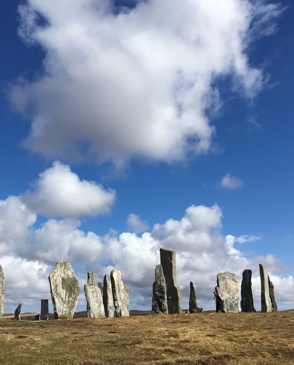 Tall, slender standing stones against a blue sky with scattered clouds.
