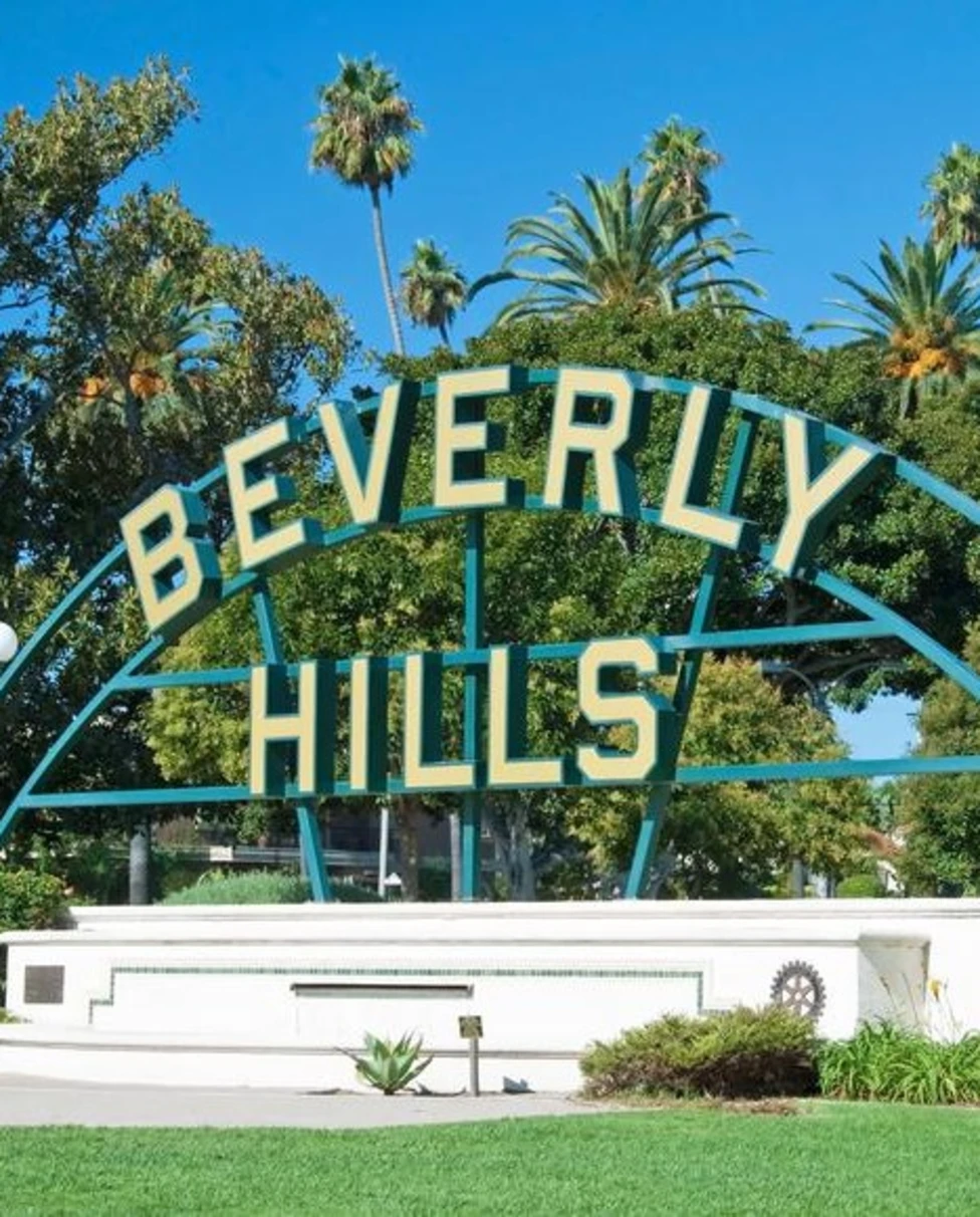 Beverly Hills signage at Beverly Gardens Park with palm trees and a clear sky in the distance.