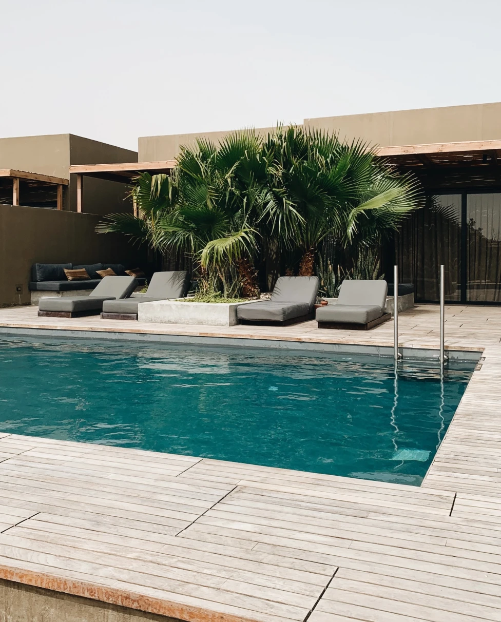 Pool and deck with lounge chairs and tall plants on cloudy day