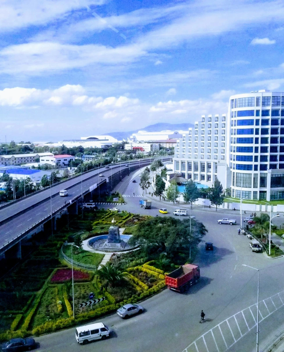 Aerial view of Addis Ababa, with gardens underneath a freeway and buildings and trees in the distance.