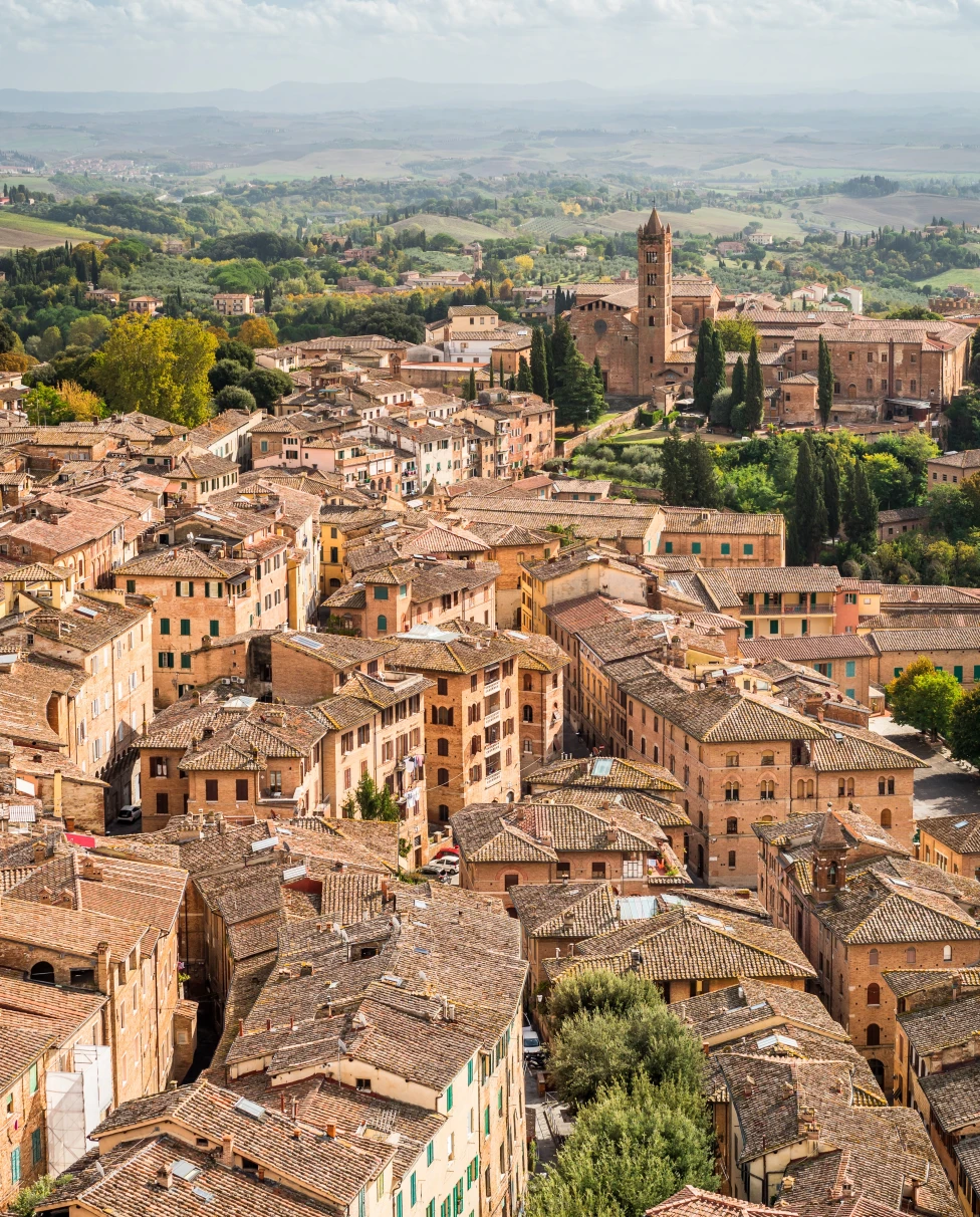 The tan and orange colorful town of Lucca with green trees immersed throughout in Tuscany, Italy.
