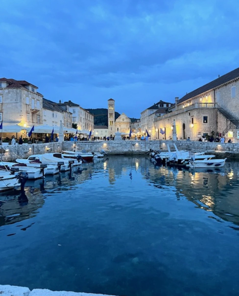A picturesque twilight scene of a town by the water, with buildings casting reflections on the calm surface.