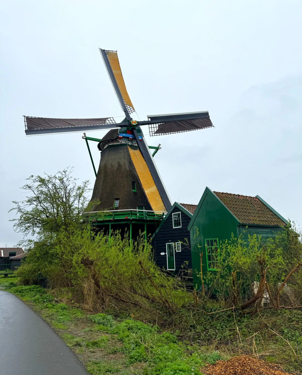 A picturesque countryside scene with a traditional windmill and adjacent green structure under an overcast sky.