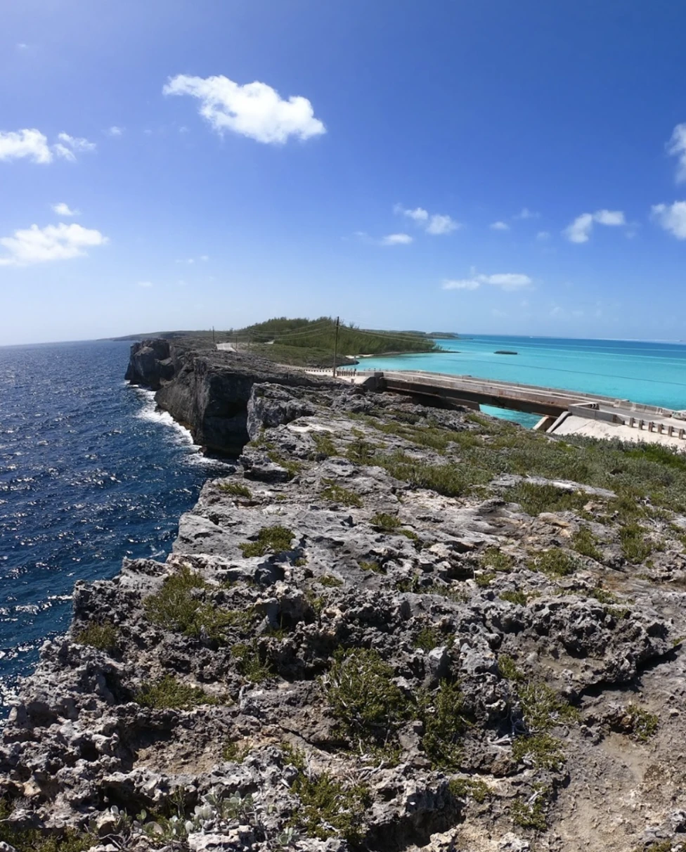A view of blue water near a rocky shoreline and bridge during the daytime.