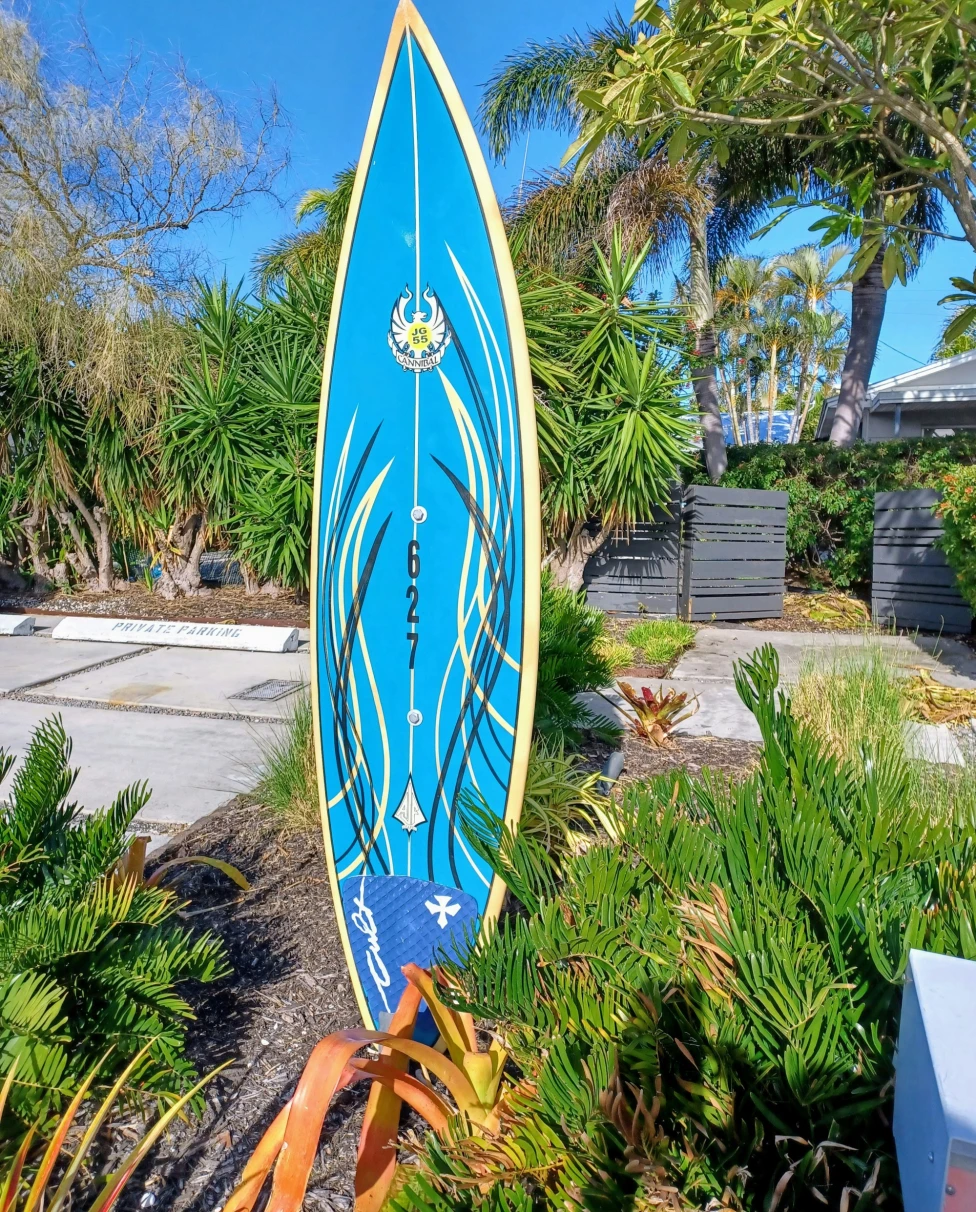 A blue surfboard standing up in an outdoor garden during the daytime